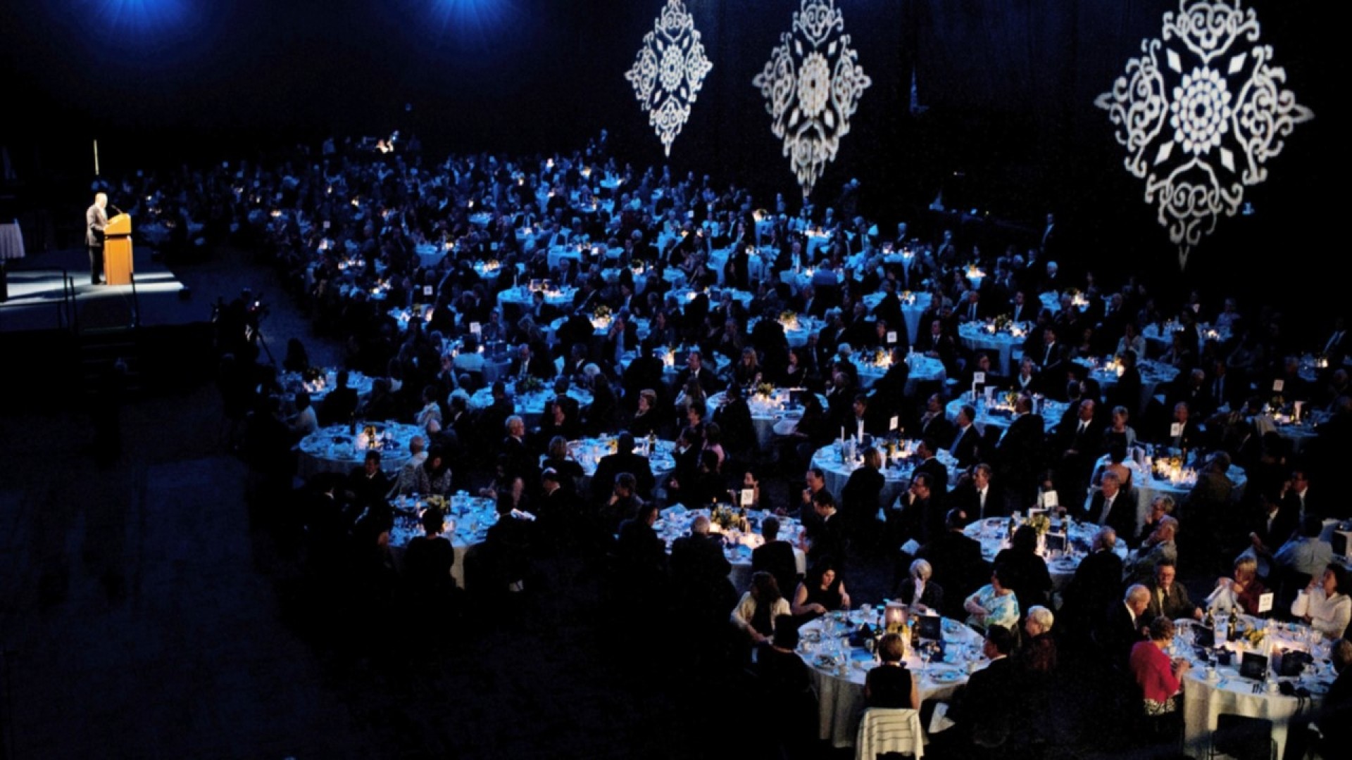 Dark banquet hall with hundreds of guests sitting at round tables