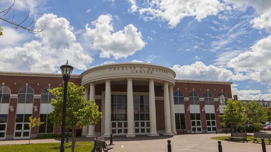 Exterior of the Charles V. Keating Centre main entrance on a sunny day with some clouds.