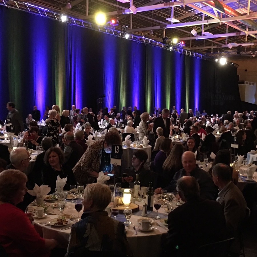 Dim lit banquet room with people sitting behind round tables