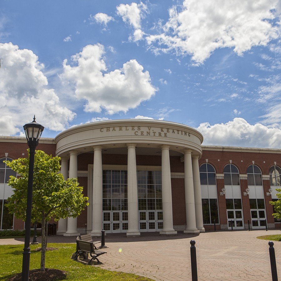 Exterior of the Charles V. Keating Centre main entrance on a sunny day with some clouds.