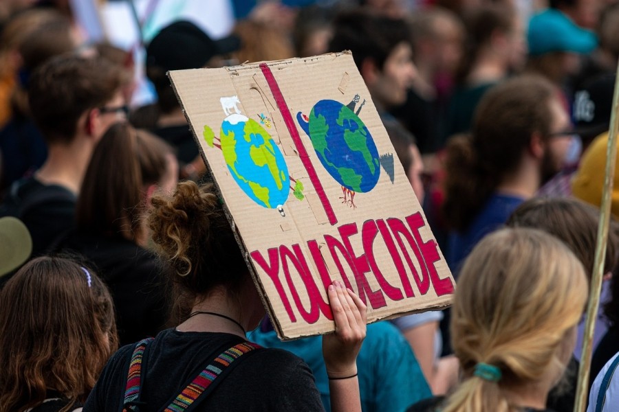 Climate protestor holding a sign with two planet Earths depicted, one seemingly ruled by corporations, and the words "You Decide" underneath